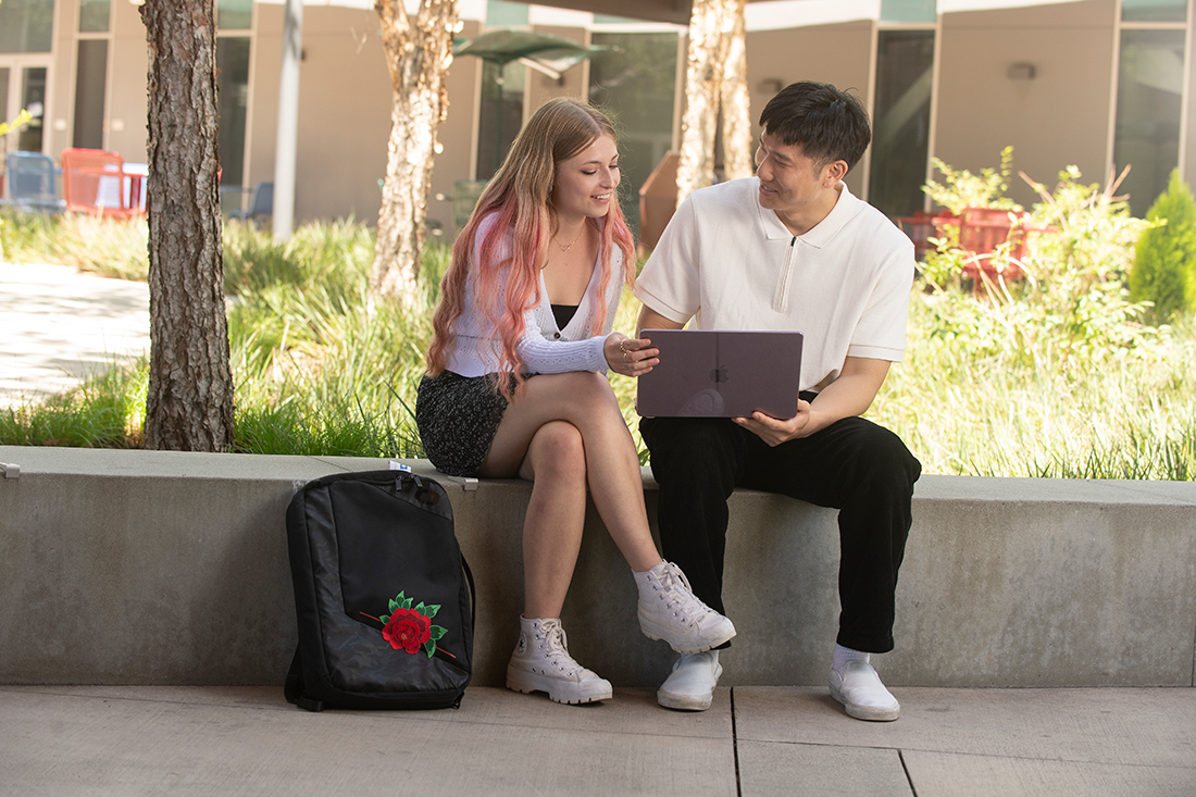 A female and male student look at a laptop together. 