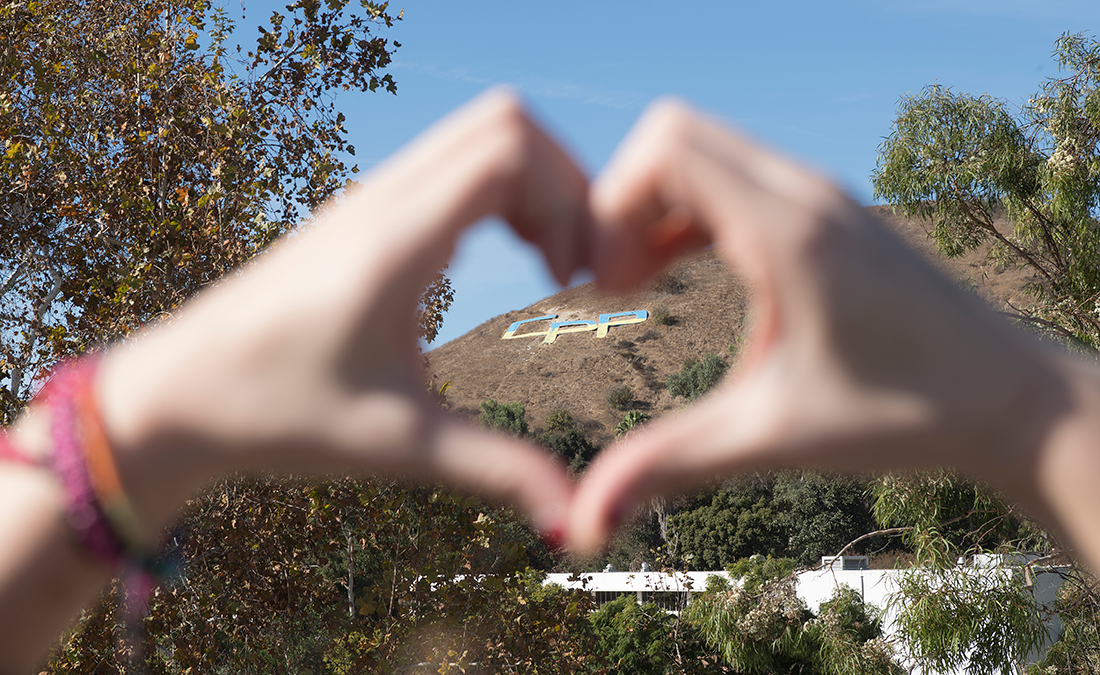 A person makes a heart with their fingers making it shape around the CPP letters in the background.