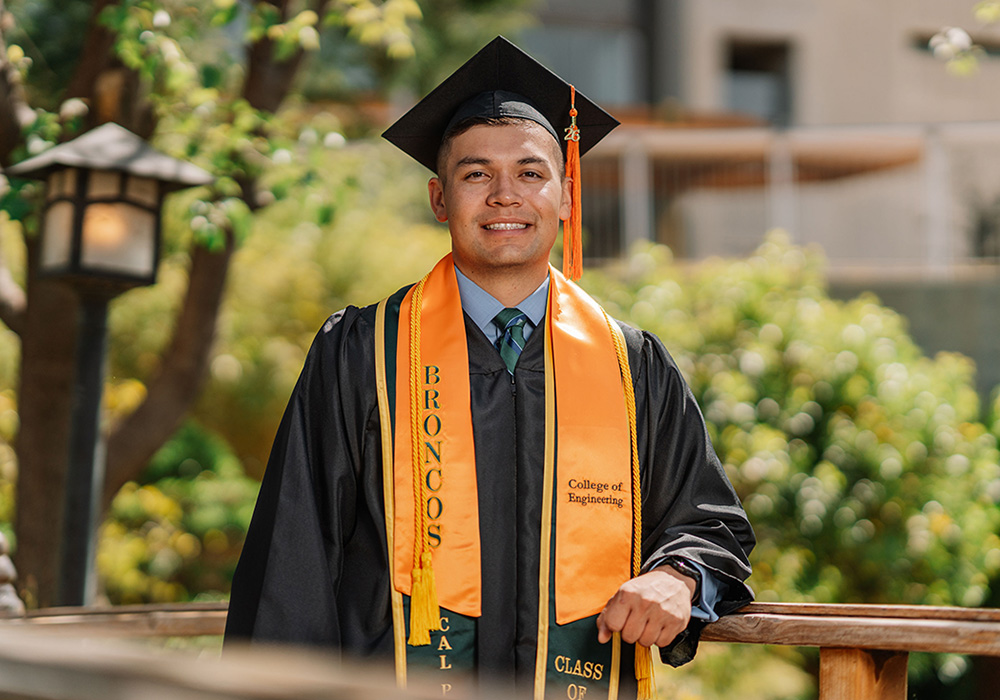 Justin Mills smiles in graduation regalia at the Aratani Japanese Garden. 