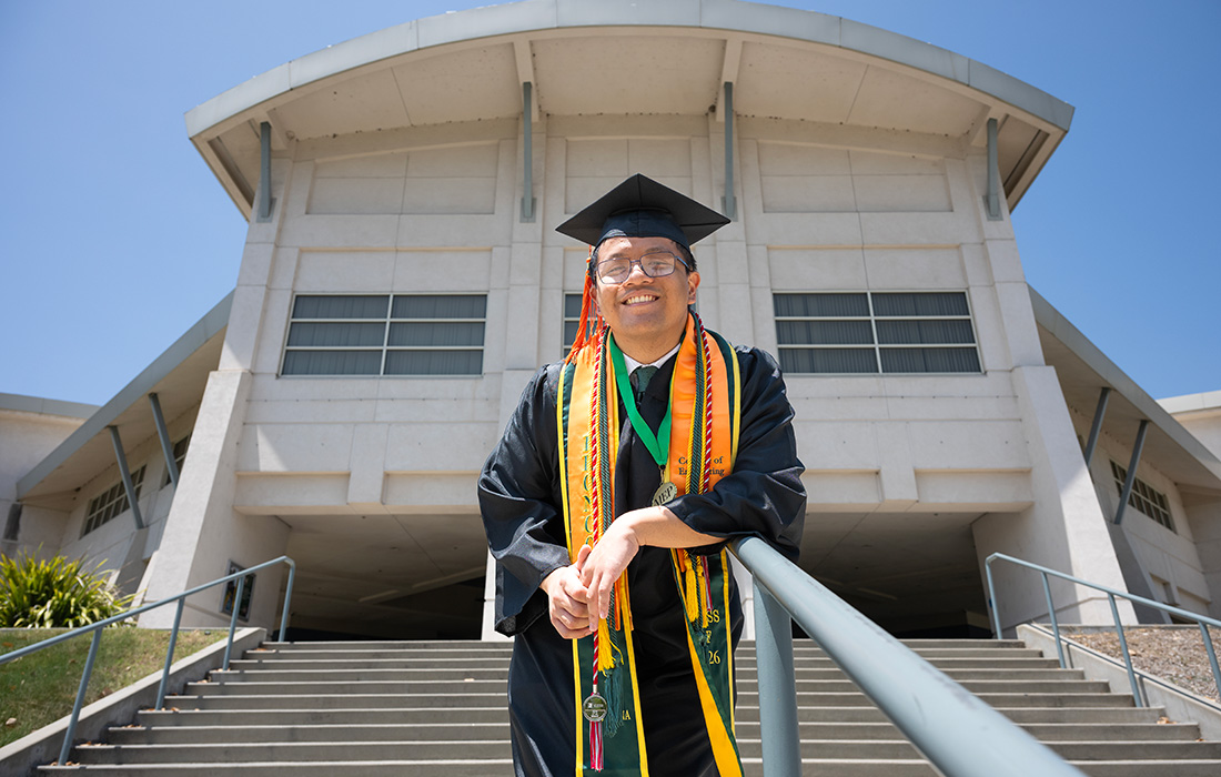 Tristan Obordo smiles in graduation regalia on the steps on the College of Engineering
