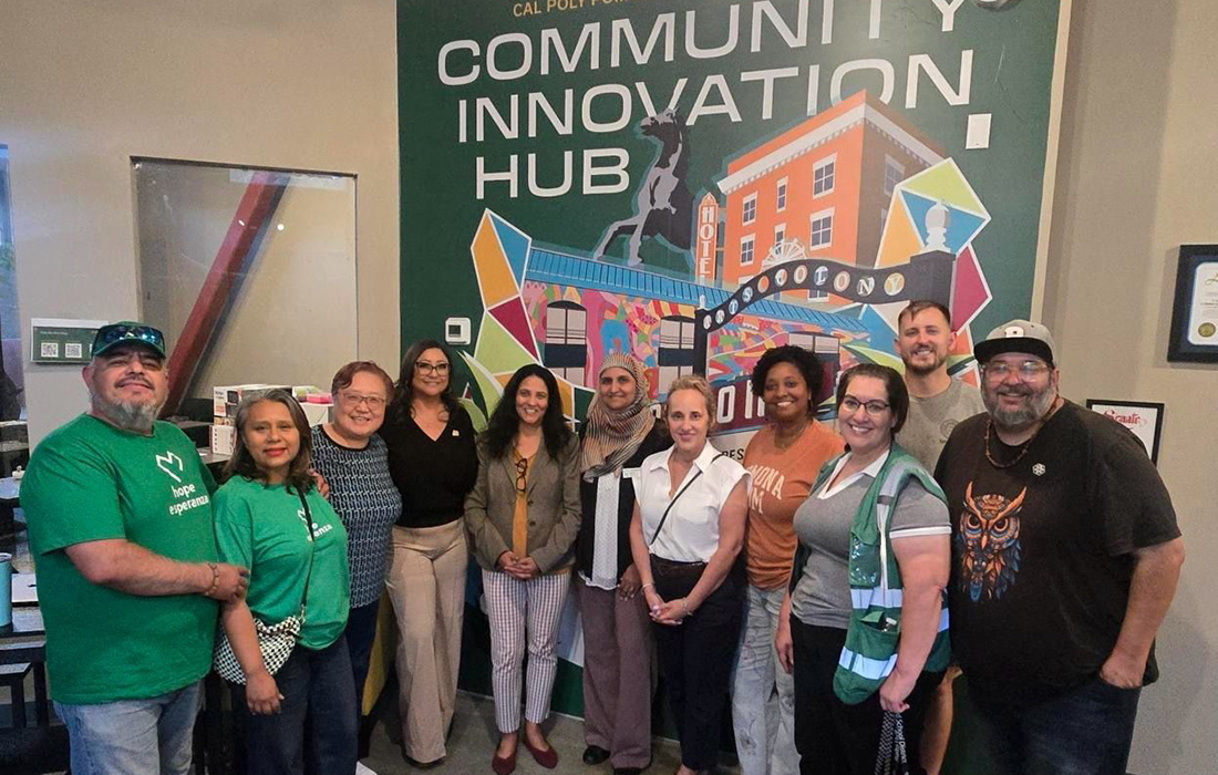 Community members smile in front of a mural that says Comnunity Innovation Hub.