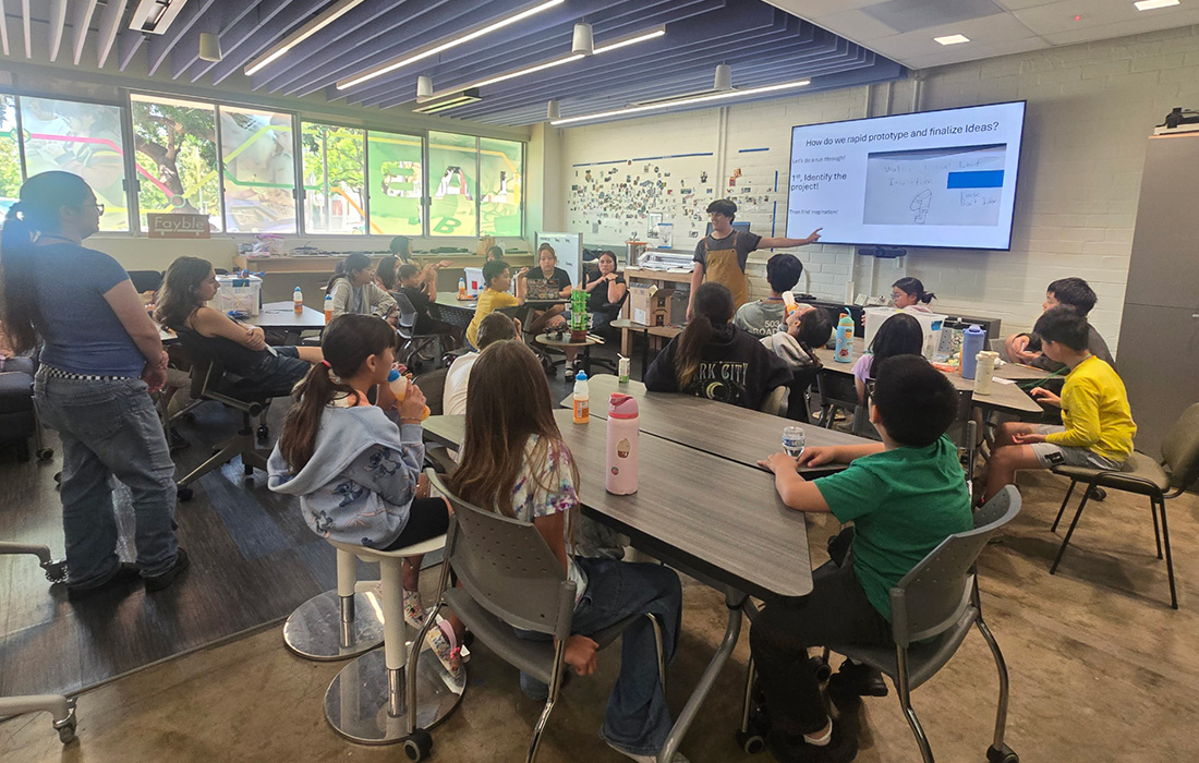 A group of students sit at tables during a presentation titled How do we rapid prototype and finalize ideas?