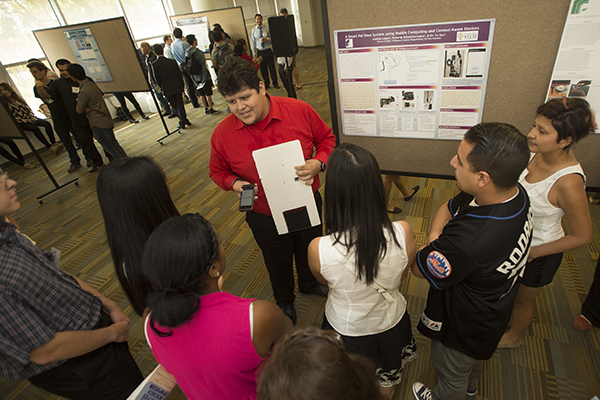 Student in a red shirt explaining his research to a small audience
