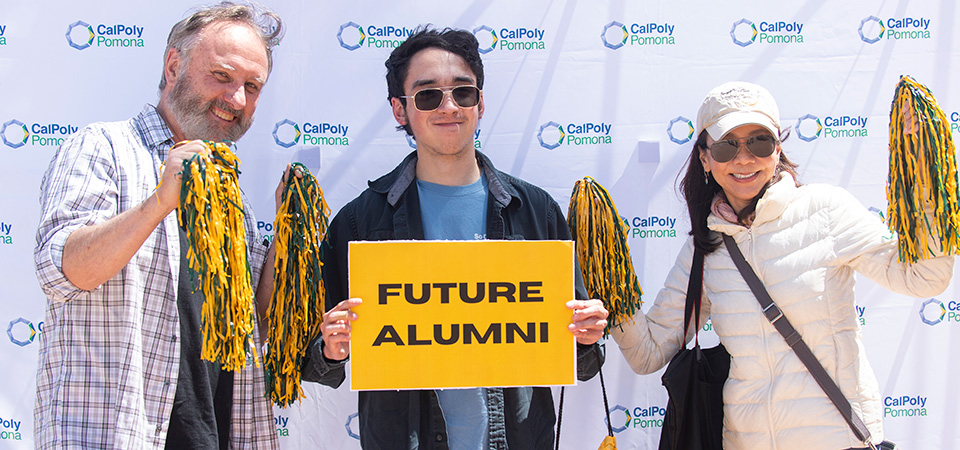 A prospective student holds up a "Future Alumni" sign while his parents stand on either side of him