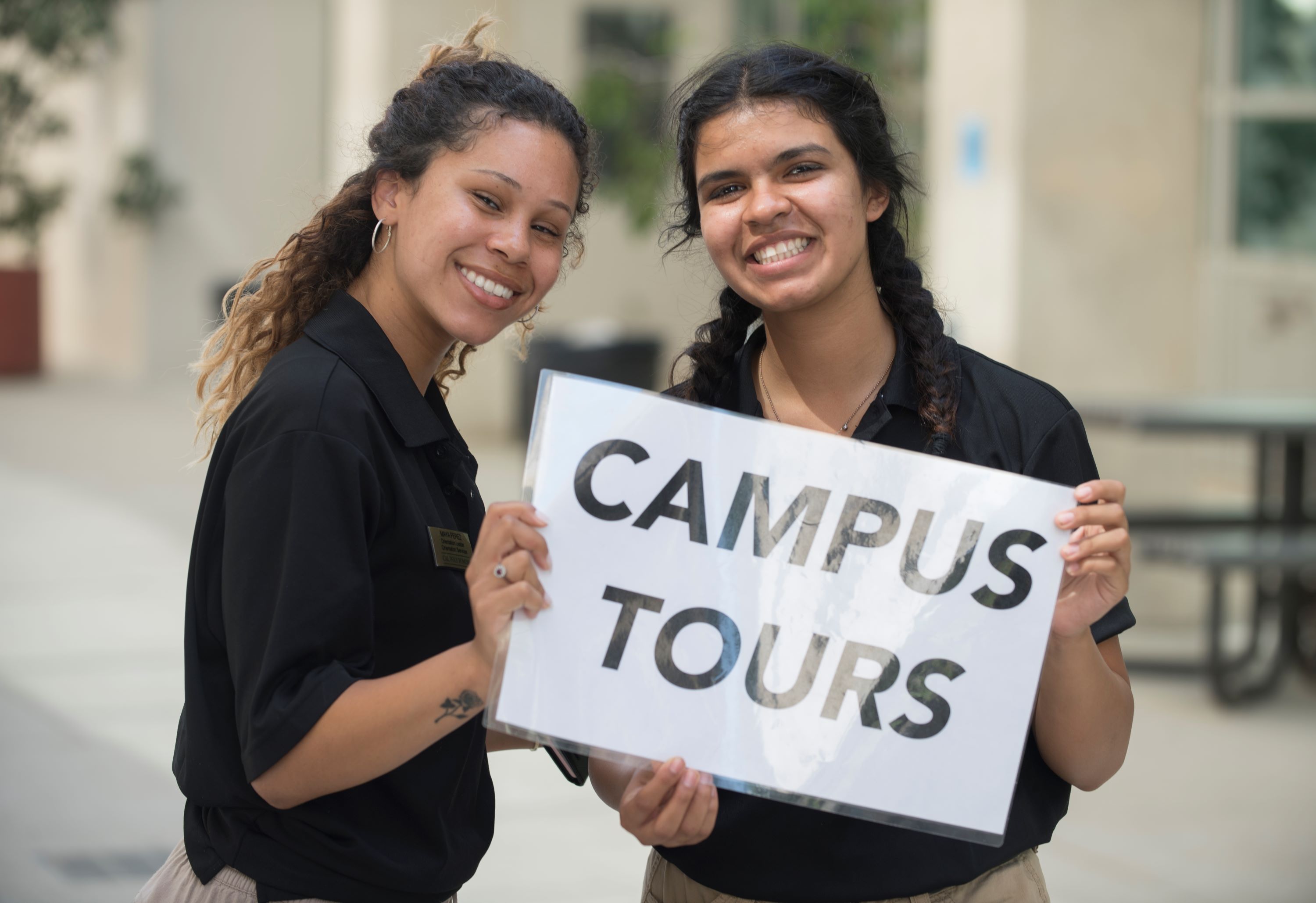 Two female tour guides holding a Campus Tour sign