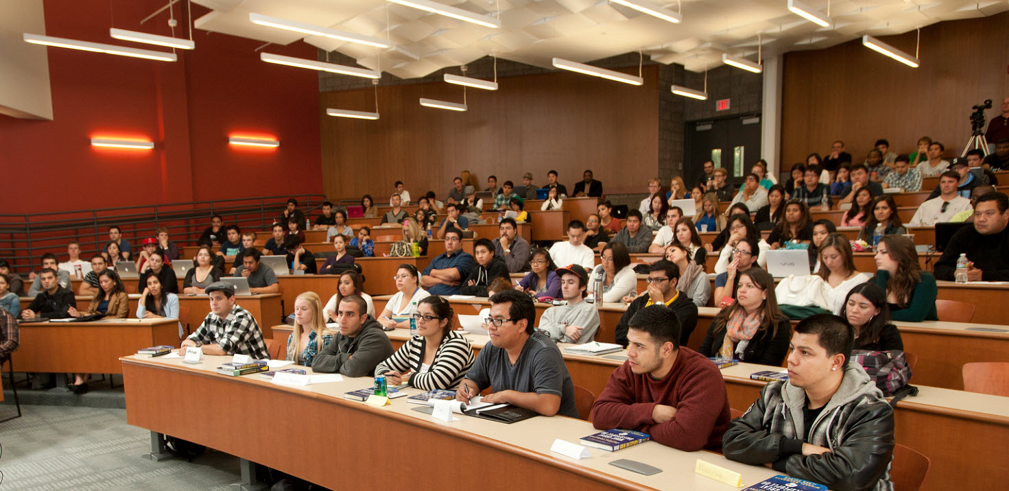 Photo of students in a classroom listening to a panel of professors lecture.