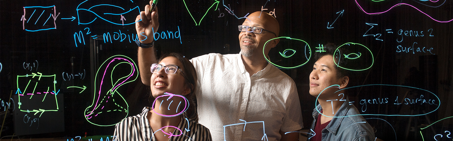 Professor and two students working on a math board.