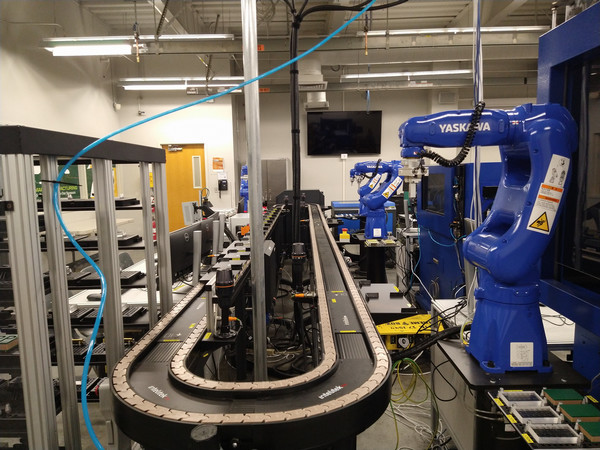 Automation lab with industrial robotic arms, conveyor systems, and smart manufacturing equipment in a teaching environment.
