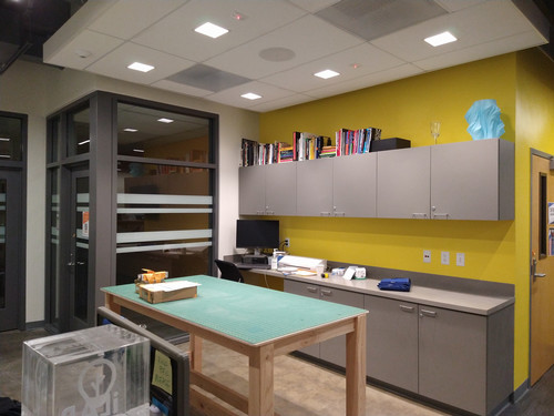 Workstation area in the iLab featuring built-in cabinets, a central work table, and a ceiling with recessed square lights above a bright, functional workspace.