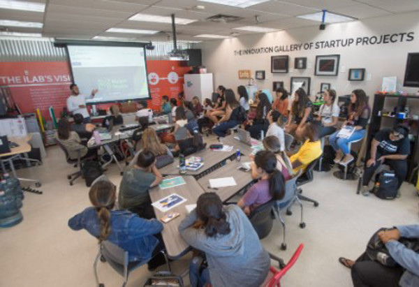 Students seated around tables in the iLab attending a presentation in a collaborative learning space