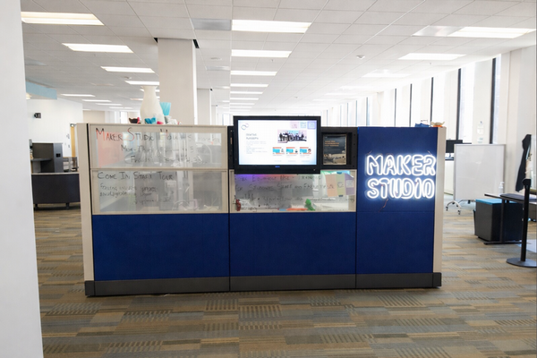 Maker Studio with a central display area, digital screen, and illuminated signage in an open, collaborative workspace.