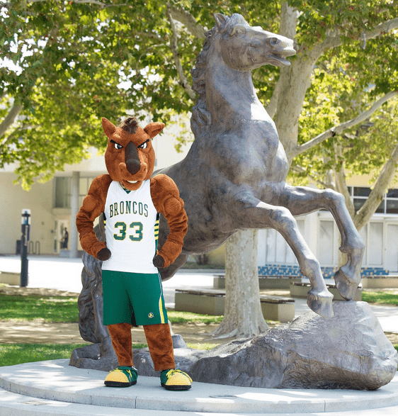 Billy Bronco poses with his hands by his hips in front of the Bronco Statue