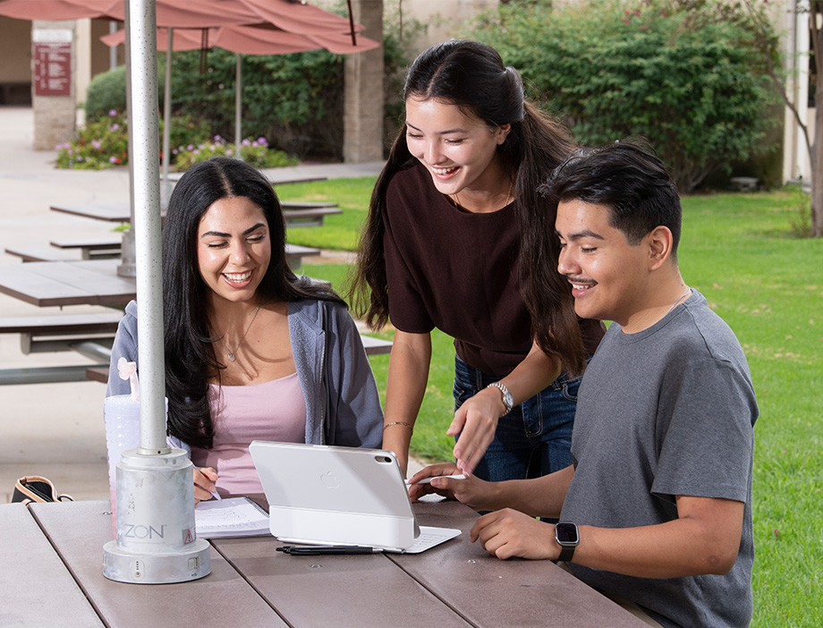 Three students looking at a laptop and smiling