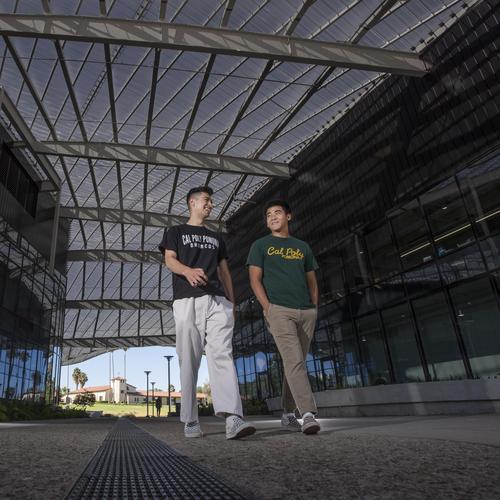 Two students walking side by side underneath the roof of the student services building.