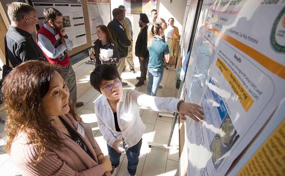 A woman points out a detail to another woman in a research poster presentation at the Cal Poly Pomona ARI Showcase.