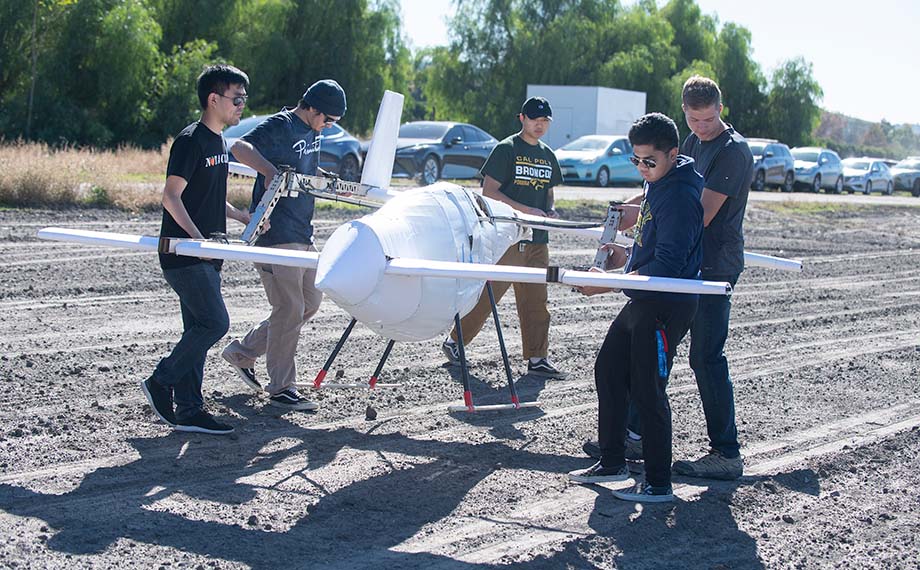 Five male students lift and move an aerial drone during research at Spadra Farm.