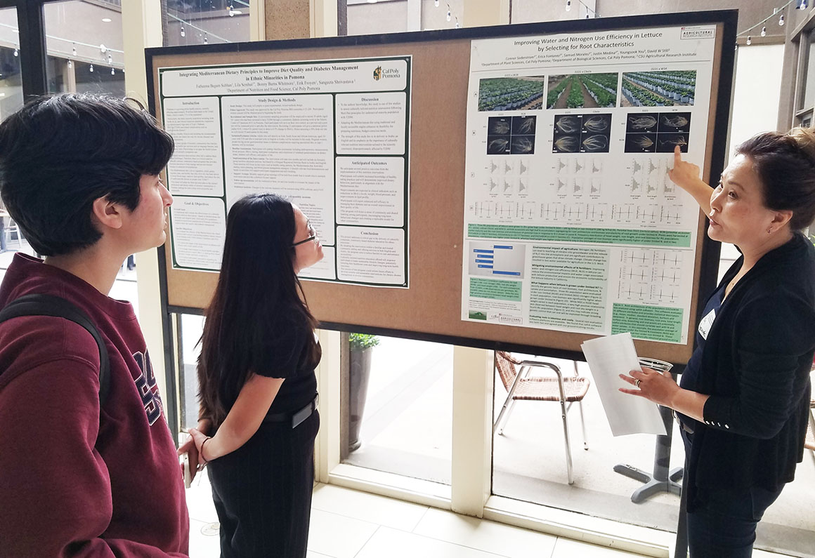 A woman gives a poster presentation to two students at the Cal Poly Pomona Agricultural Research Institute Showcase.
