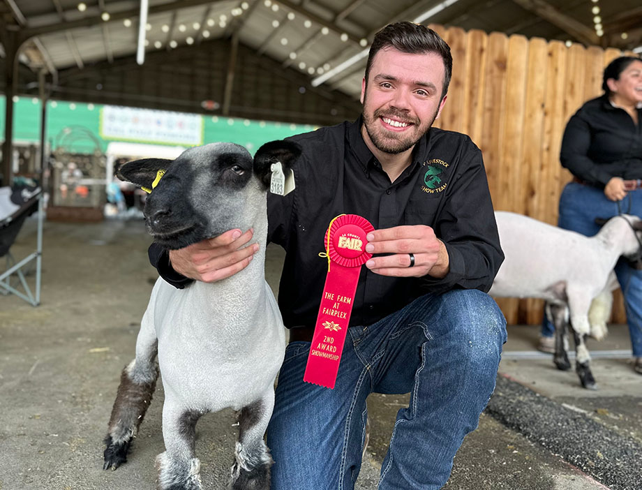 A student and sheep pose with a red ribbon they won.