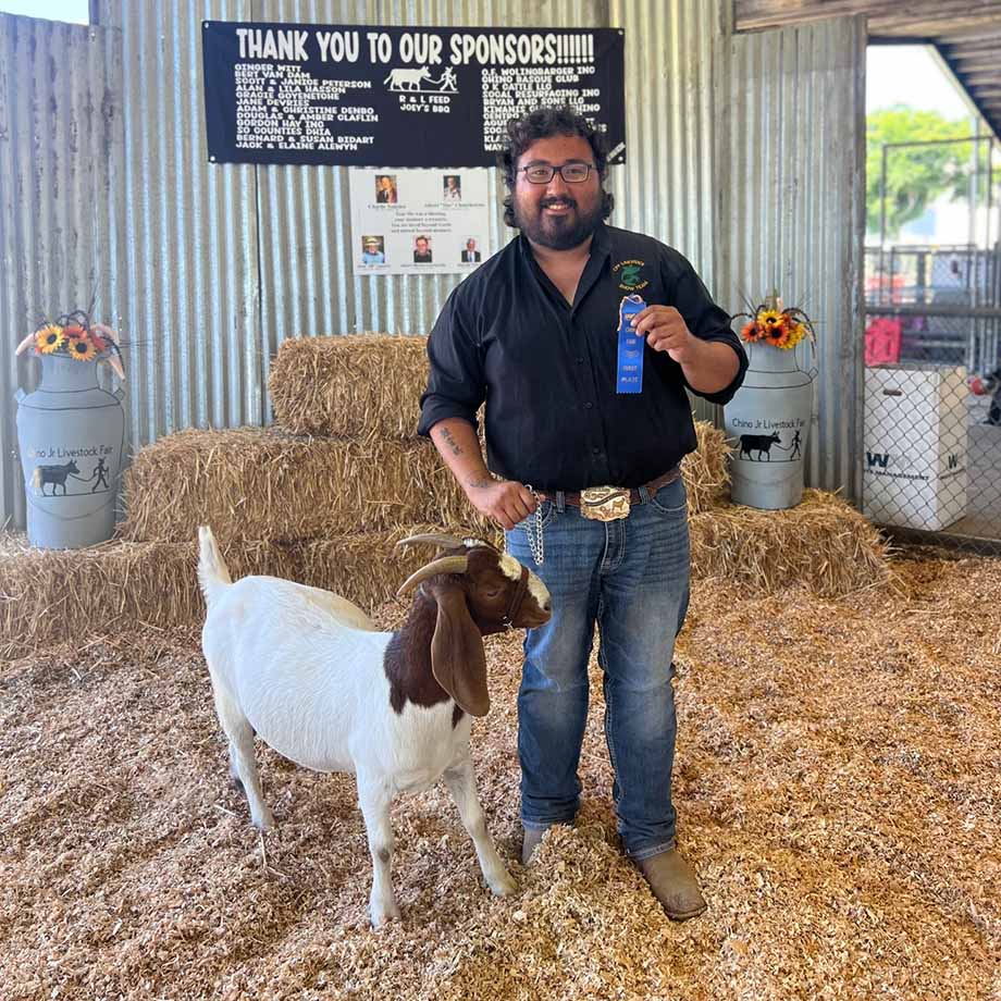A male student poses with a blue ribbon he won with his goat.