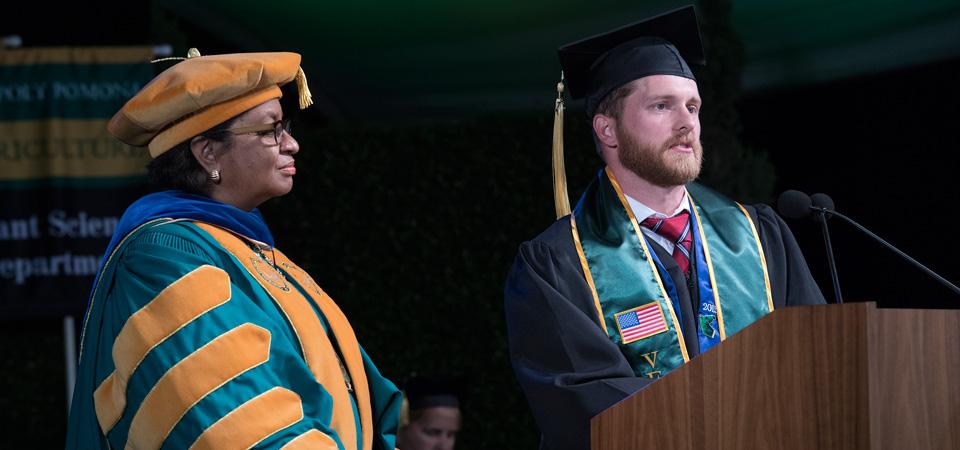 A graduating student speaks at commencement with President Coley standing alongside him