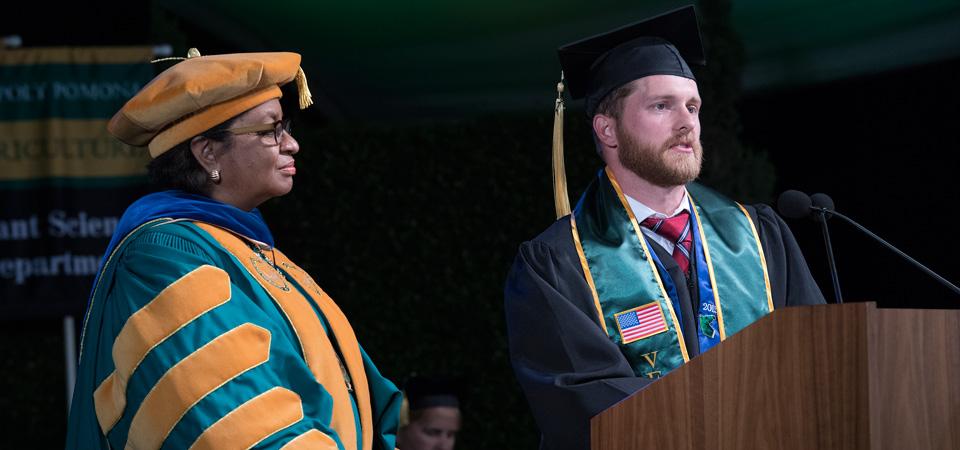 A graduating student speaks at commencement with President Coley standing alongside him