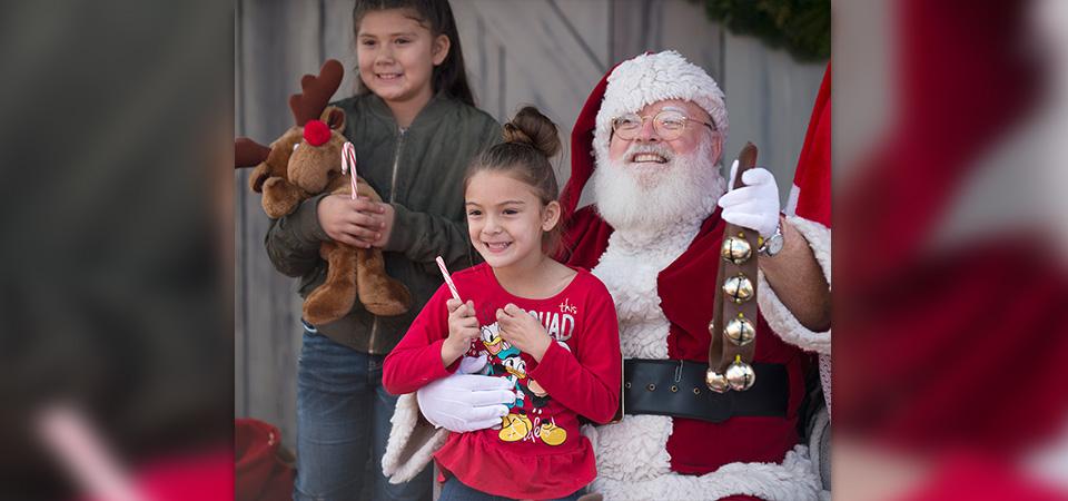 Two young girls smile and pose for a photo with Santa Claus.