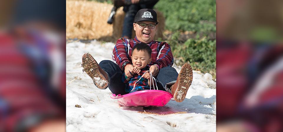 A father and his toddler son smile as they go down one of the snow slide runs.