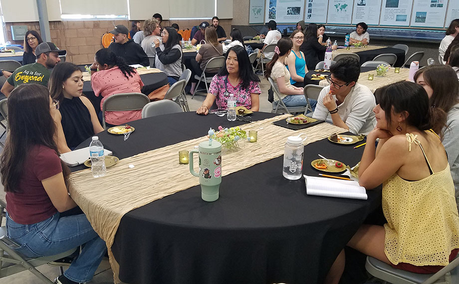 An alumna talks with students at a table.