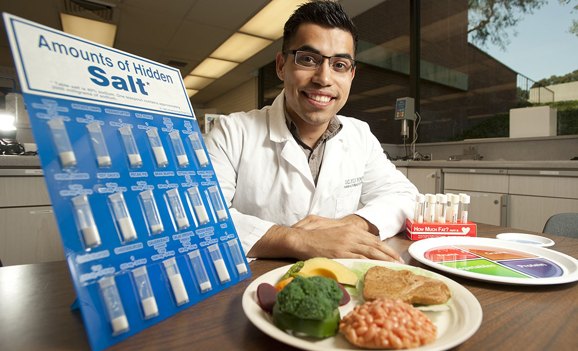 A man in lab coat poses with a display about sodium in food.