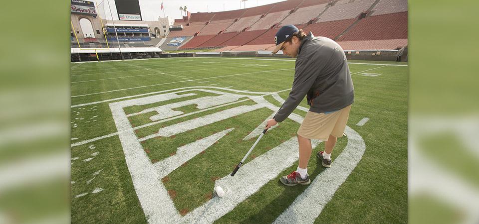 Cal Poly Pomona plant science student Sean McLaughlin paints the NFL logo at the Los Angeles Memorial Coliseum.