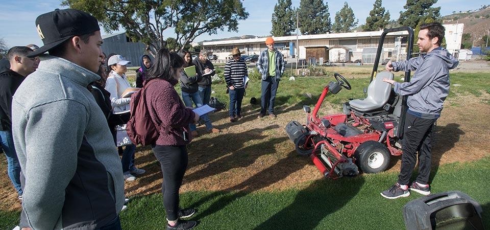 A graduate student instructs students on operating a mower.