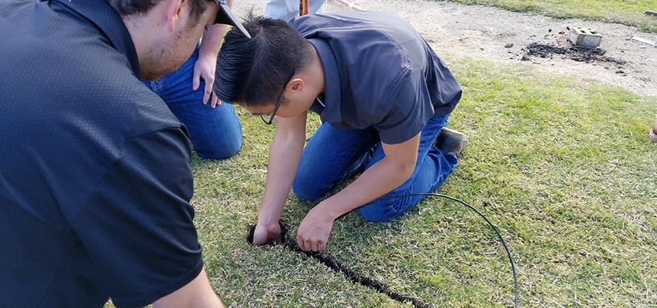 A student kneels on the turf while installing a moisture sensor.