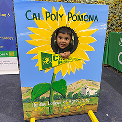 A child sticks his face through a hole in a Cal Poly Pomona "sandwich sign" type photo cutout