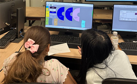 Two girls stare at a design on a computer screen