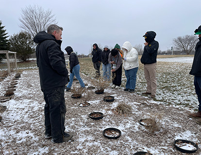 Students examine plants in the snowy ground.