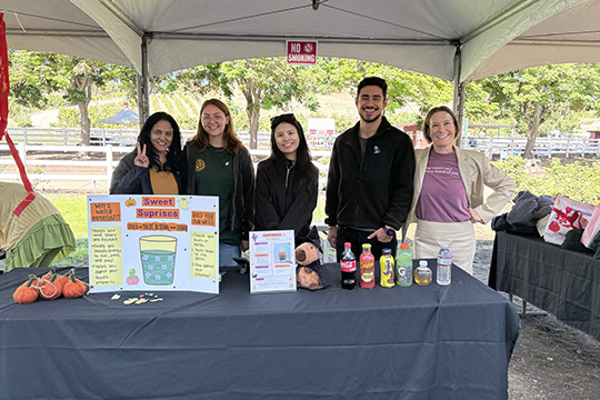 Nutrition students and faculty pose at a booth about drinks and sugar.
