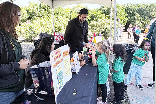 Schoolchildren line up at a booth to learn about sodas and sugar.