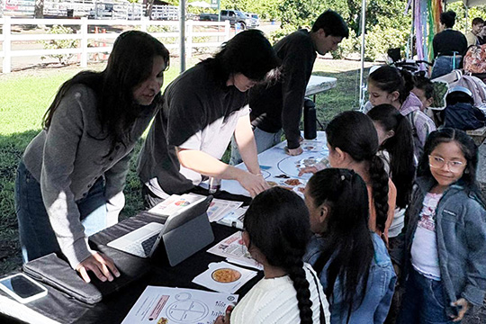 Nutrition students lean over a table to talk to schoolchildren.