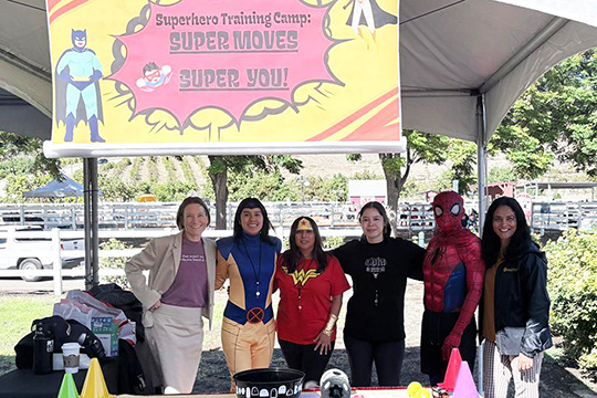 Nutrition students dressed in superhero costumes pose with faculty at a booth about exercise.