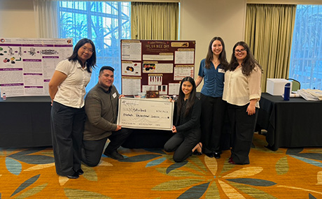 The team poses with a check in front of their poster presentation.