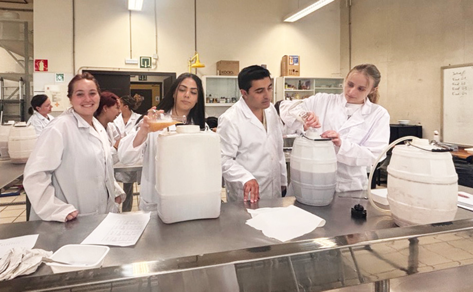 Students in lab coats working with containers and liquids.