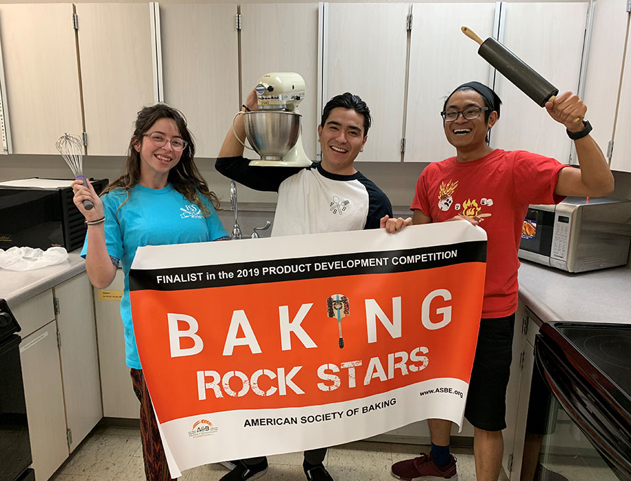A female student and two male students celebrate being named as finalists to a national baking competition.