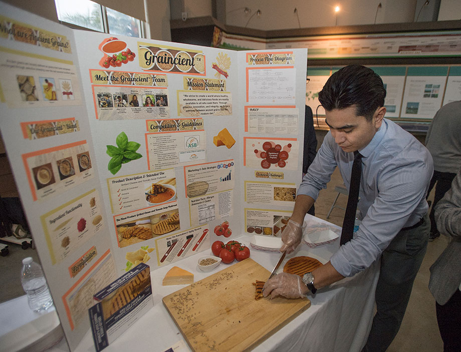 A student cuts food samples at a product presentation booth.