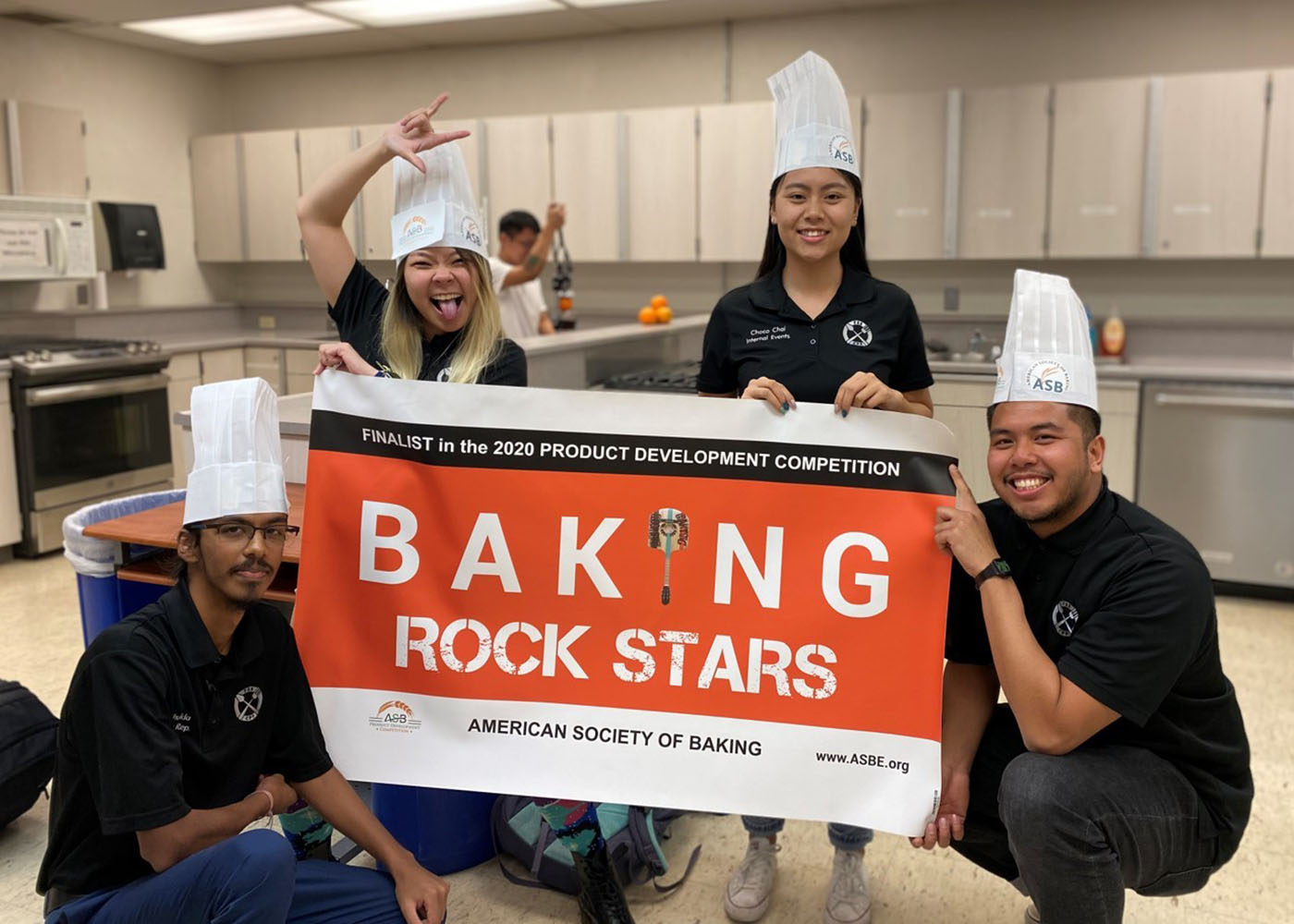 Four students posing with a banner in a kitchen 