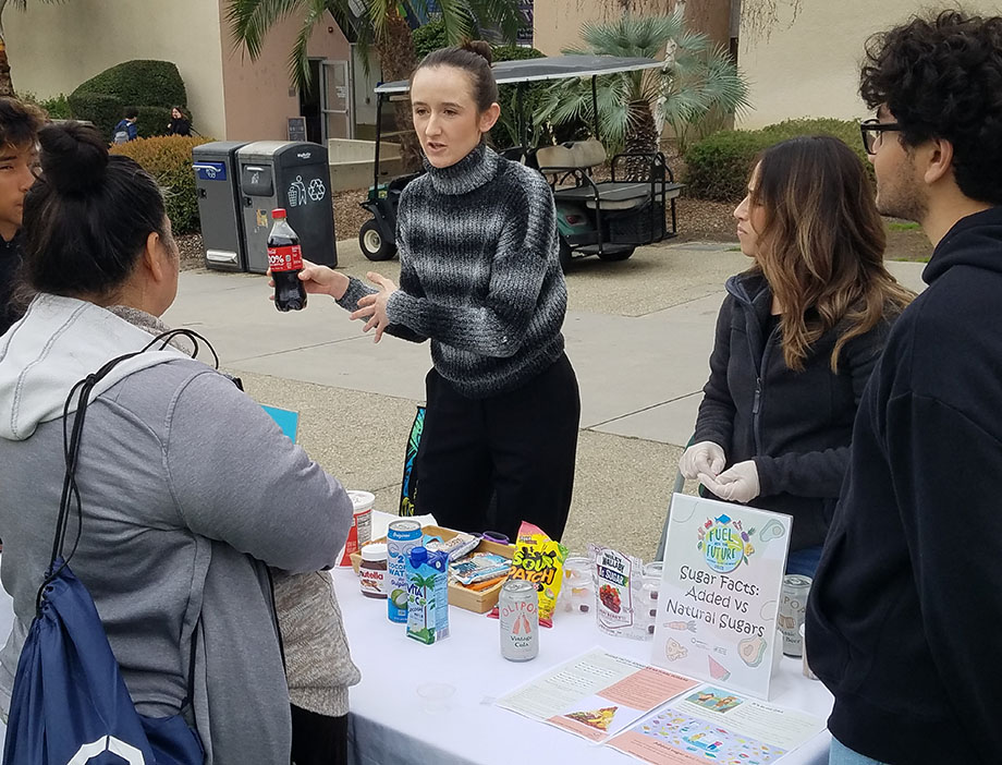 A female nutrition student educates her peers about sugar in sodas at a National Nutrition Month event.