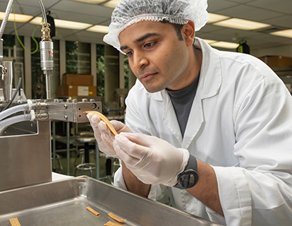 A student examines a food product extruding from a machine.