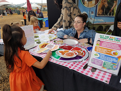A female student interacts with a young girl at a booth about nutrition. 
