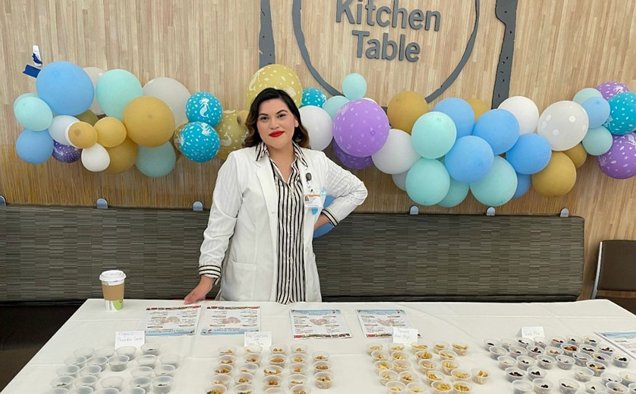 Woman in a lab coat poses at a table with food samples.