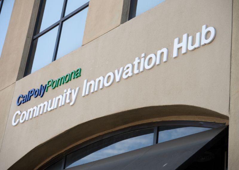he exterior sign of the Cal Poly Pomona Community Innovation Hub is displayed on a beige building with large windows.