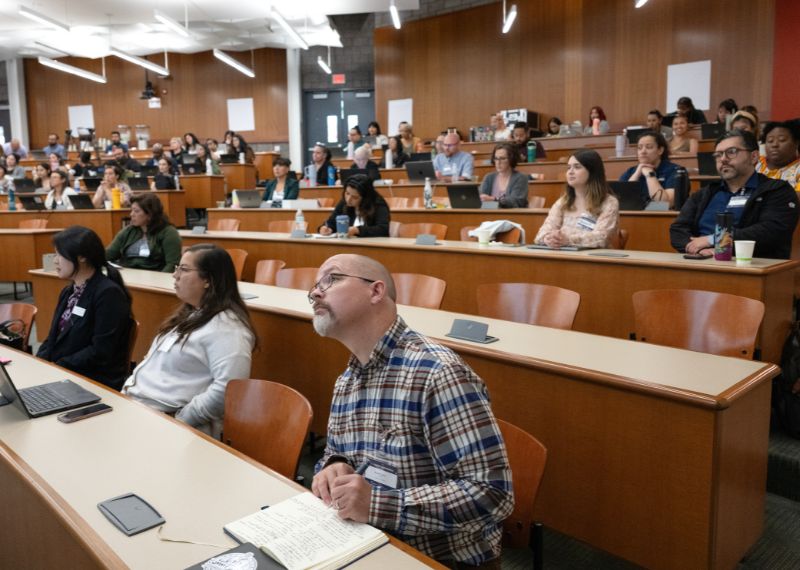 Attendees in a large lecture hall take notes and listen attentively to a presentation during a conference or seminar.